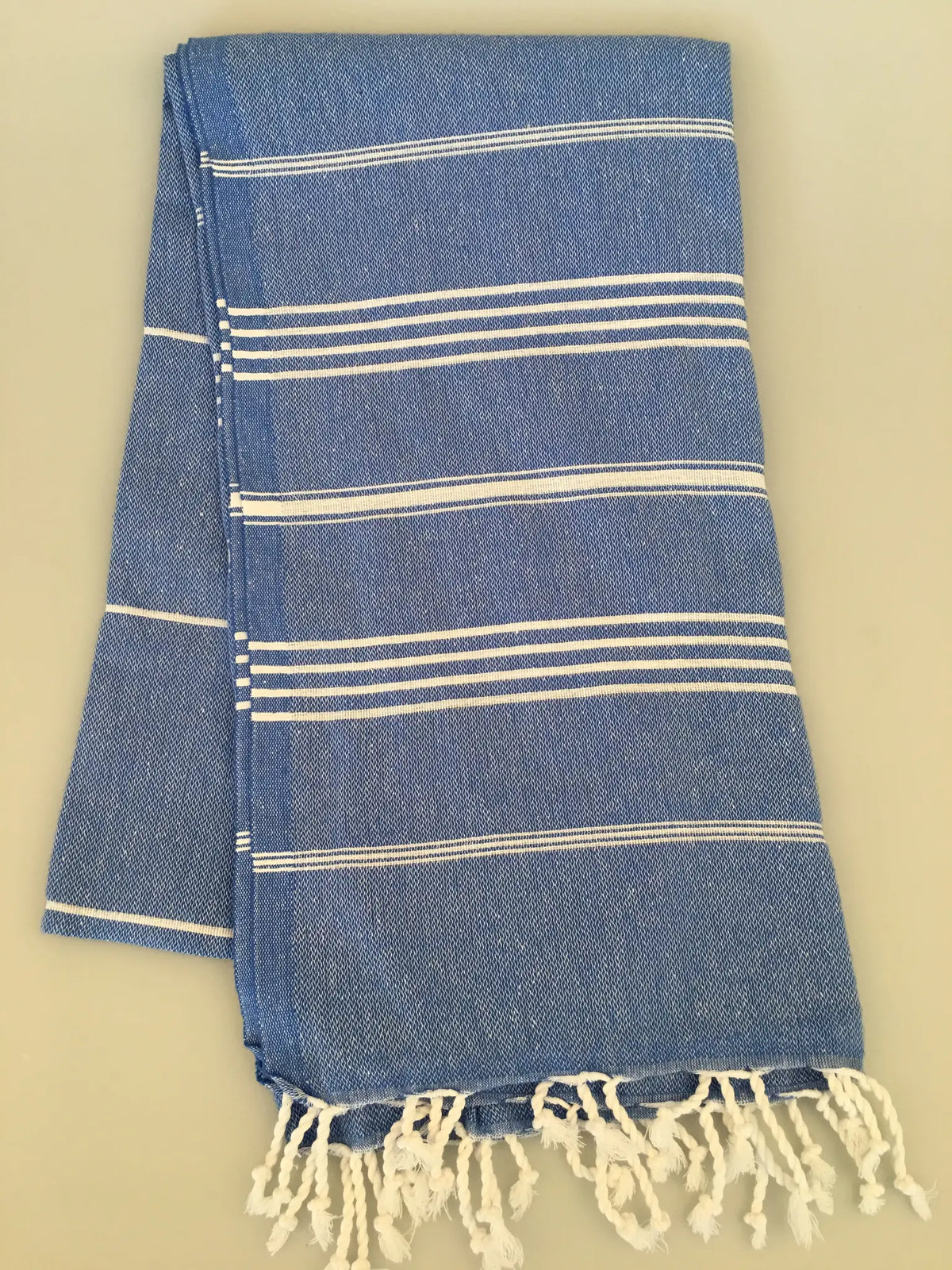 Blue and white striped Turkish towel with fringed ends, folded neatly on a light background.