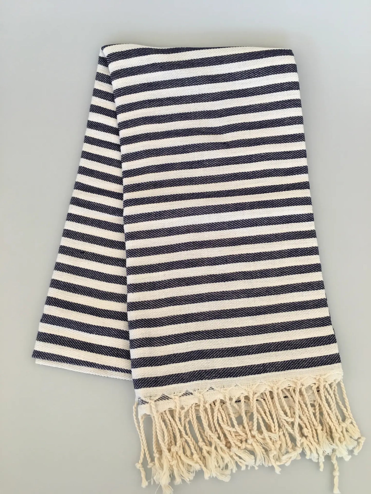 "Navy and cream striped Turkish towel with fringed edges, folded on a light gray background."