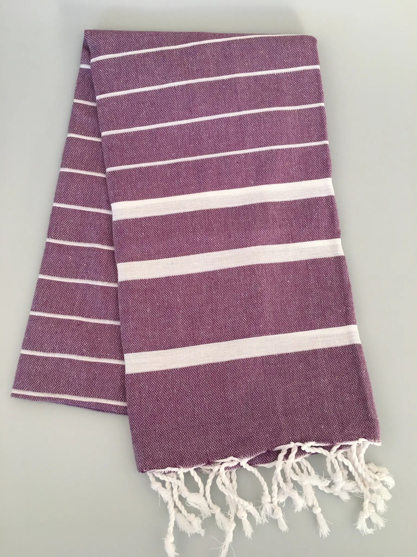 "Purple Turkish towel peshtemal with white stripes and fringed edges, flat lay on light background."