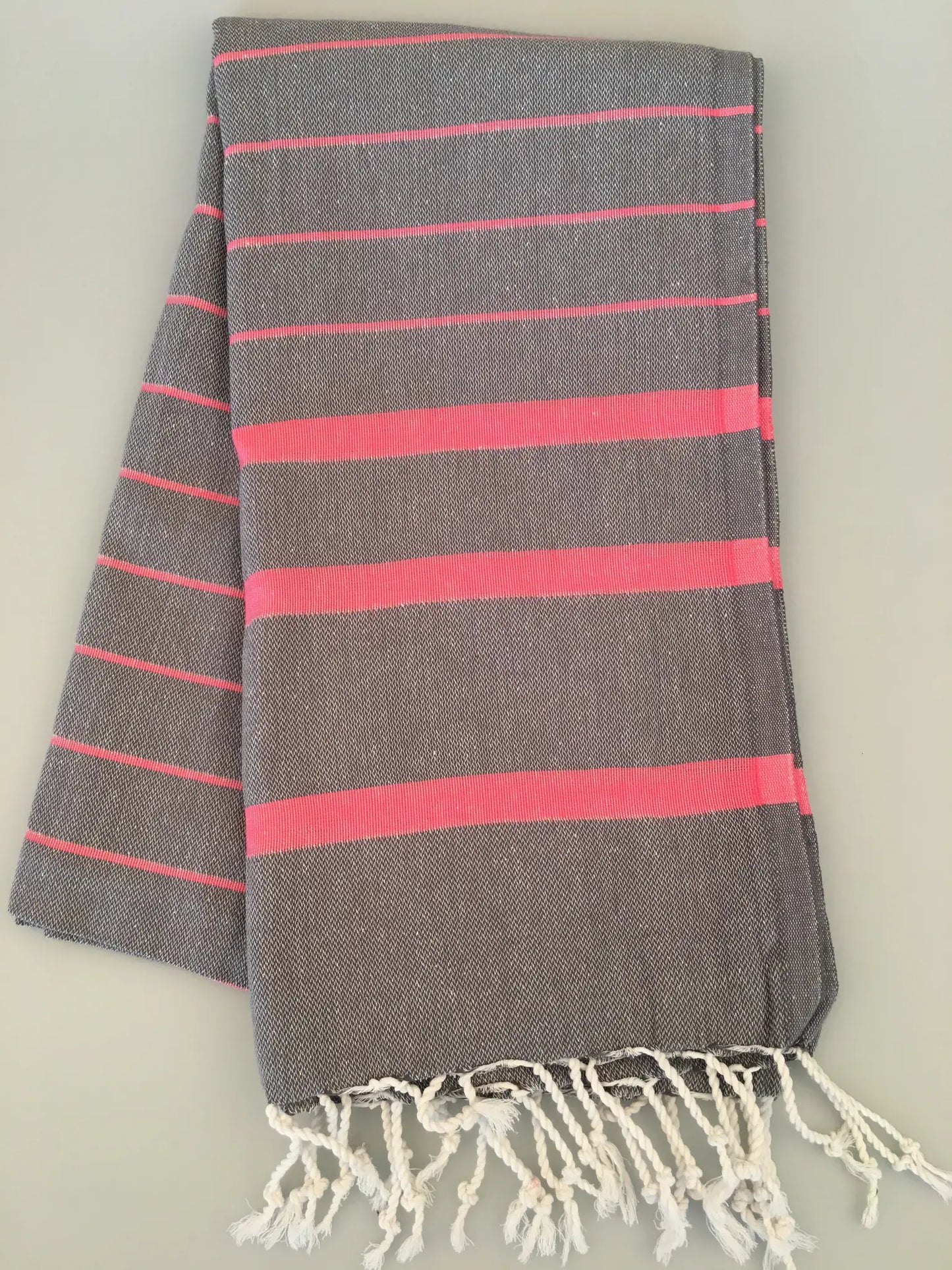 "Gray Turkish towel with pink stripes and white fringes, folded on a light surface"
