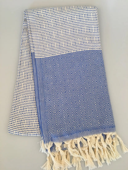"Lycia Patara Turkish towel in blue and white with diamond patterns and fringed edges, laid flat on a light surface."