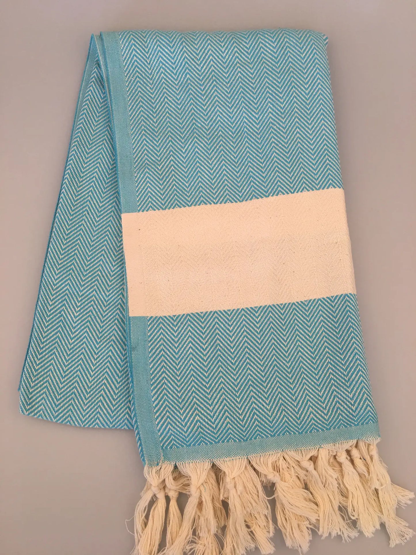 Turquoise Turkish towel peshtemal with herringbone pattern and cream striped band, featuring fringed edges.