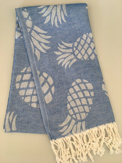 Blue Turkish towel with white pineapple jacquard pattern and fringed edges, folded on a light background.