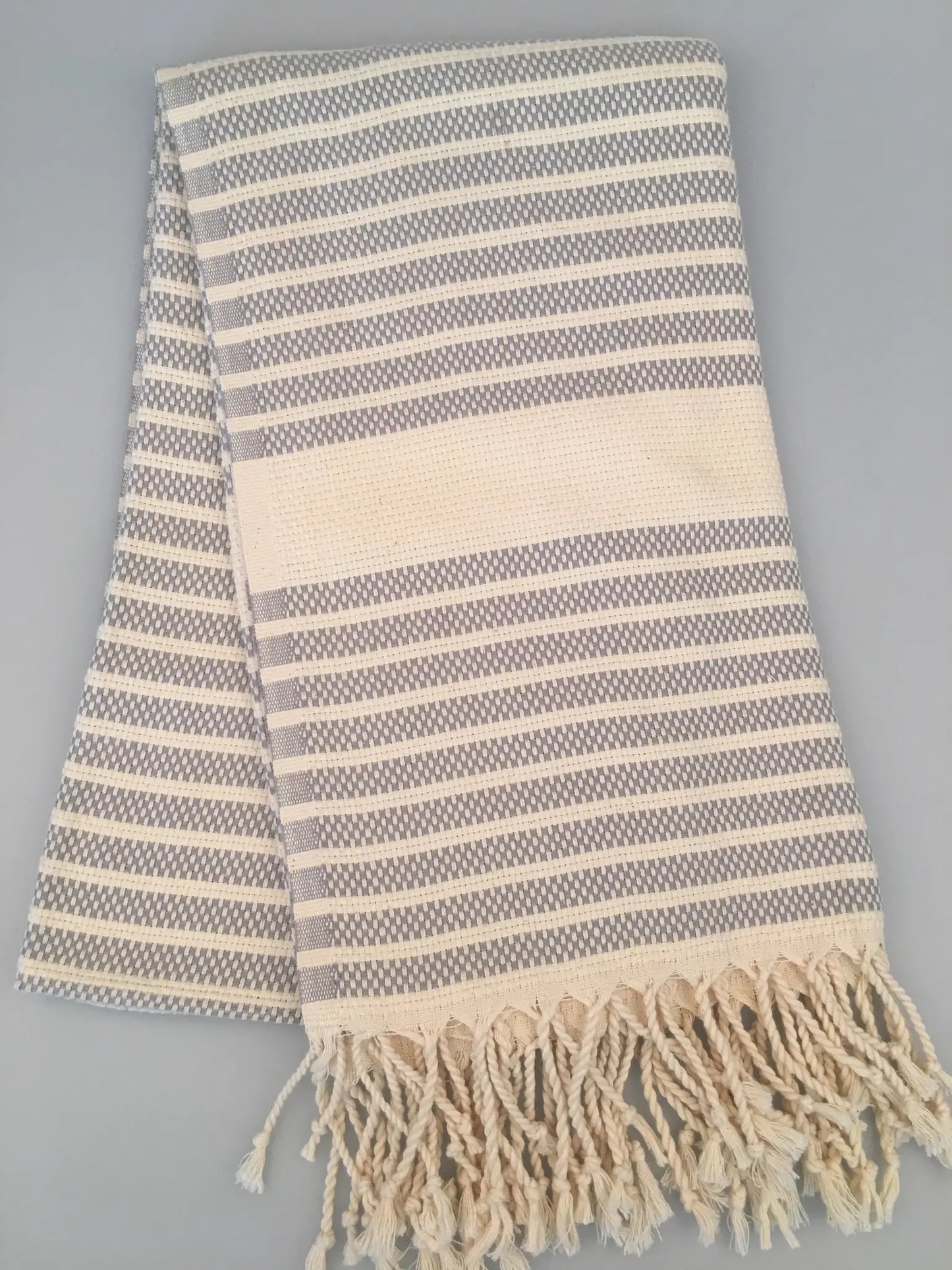 Hittite Turkish towel in gray and cream with striped pattern and fringed edges, laid flat on a gray background.