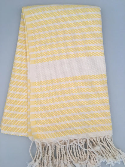 "Yellow and white striped Hittite Turkish towel with fringed edges, folded on a light gray background."