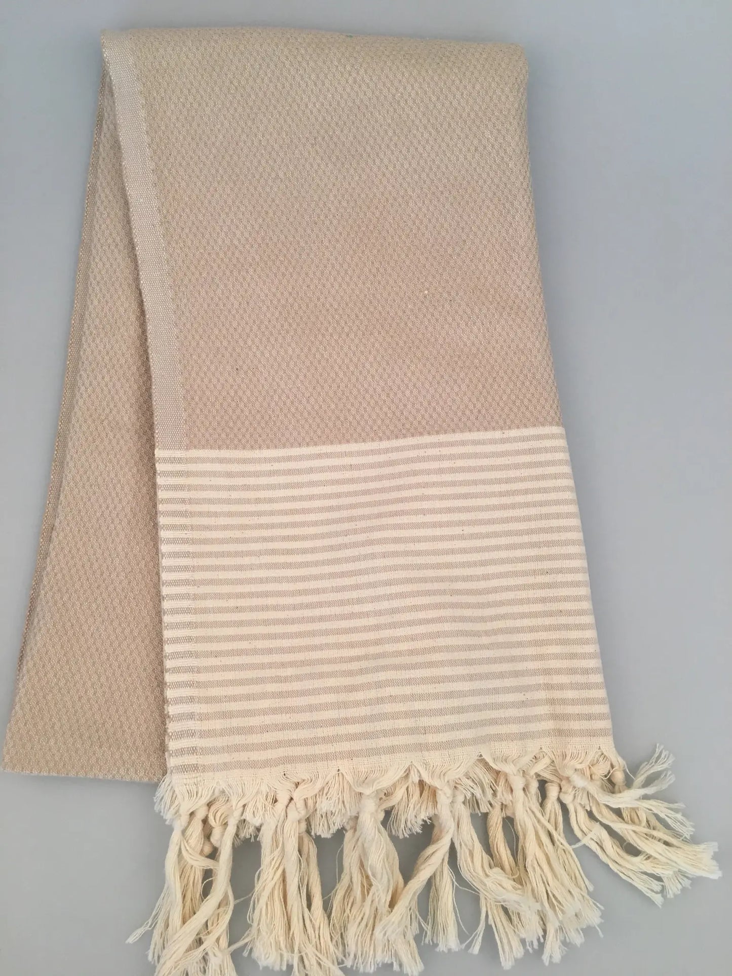 "Beige Miletus Turkish towel with textured weave and striped hem, featuring fringed edges, laid flat."