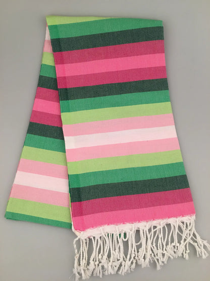 "Striped Turkish towel in pink, green, and white with fringe edges, folded on a gray background."