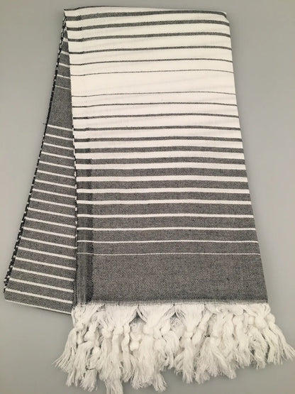 "Telmessos Turkish towel peshtemal in gray and white stripes, featuring fringed edges, laid flat on a light background."