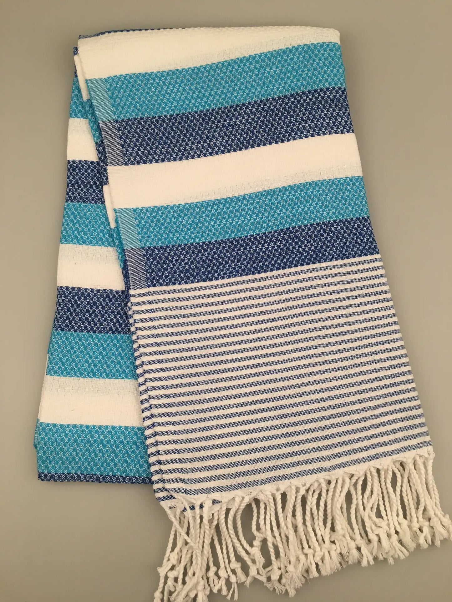 Turquoise and white striped Turkish towel with a textured pattern and fringed edges, folded on a light gray background.