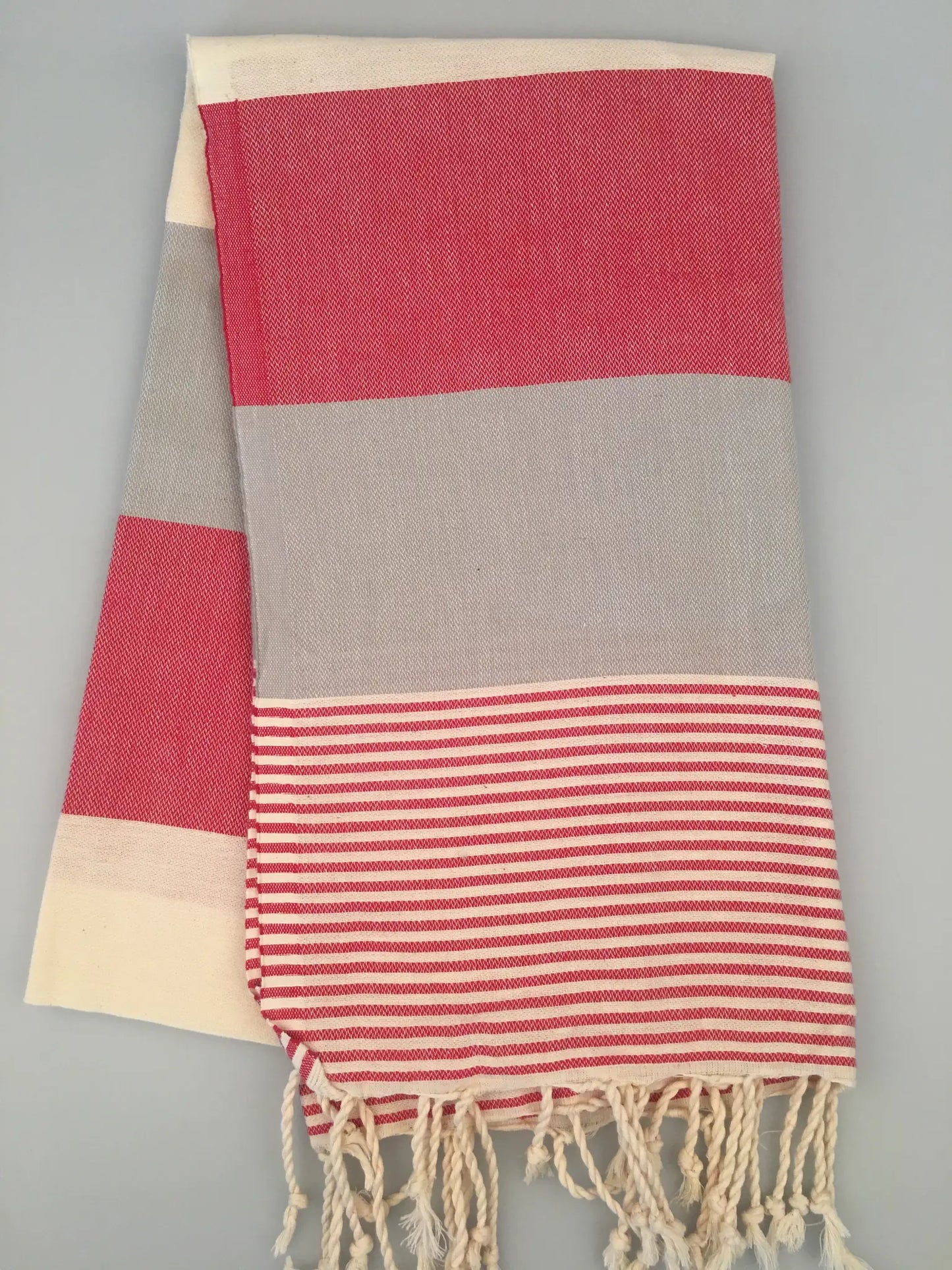 "Red and gray striped Lagina Turkish towel peshtemal with fringe, folded on a light gray background."