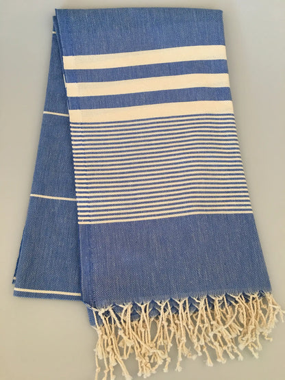 "Blue and white striped Turkish towel with fringed edges, folded neatly on a light background."