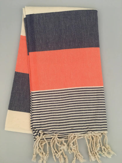 "Striped Lagina Turkish towel peshtemal with navy, coral, and cream sections, fringed edges, laid flat on a light background.
