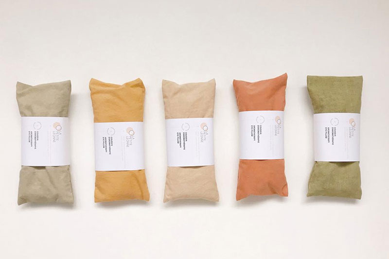 Five wrapped bundles in soft, muted colors—green, beige, orange, and two shades of light green—each secured with a white labe